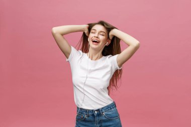 Yaşam tarzı kavramı. Pembe arka planda müzik dinlemek için telefonu kullanan genç bir kadın.