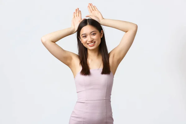 Lüks kadınlar, parti ve tatil konsepti. Sevimli ve kawaii Asyalı bir kadın, mutlu bir şekilde gülümsüyor ve ellerini başının üstüne koyup tavşan kulağı yapıyor. — Stok fotoğraf