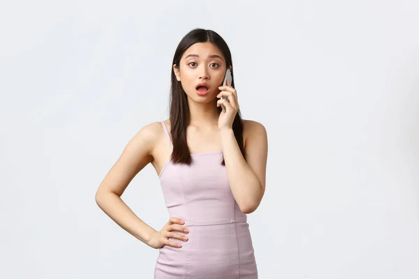 Lüks kadınlar, parti ve tatil konsepti. Şaşırmış ve şok olmuş Asyalı kadın telefon görüşmesi yapıyor, birini arıyor ve dedikodu yapıyor, beyaz arka planda duruyor. — Stok fotoğraf