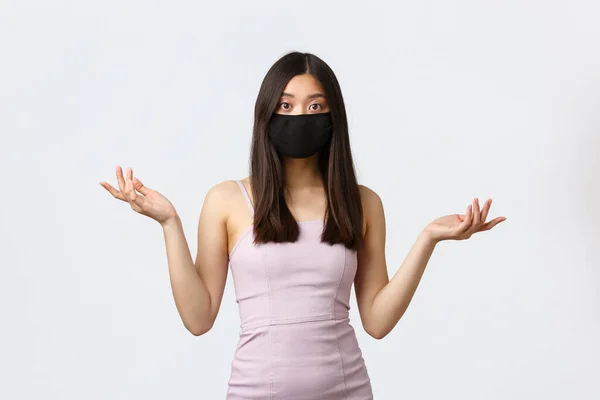 Covid-19, sosial jarak karantina dan konsep rekreasi. Wanita asia bingung dalam pakaian pesta malam dan masker wajah, tidak bisa mengerti apa yang terjadi, mengangkat bahu dengan tangan ke samping, terlihat bingung — Stok Foto