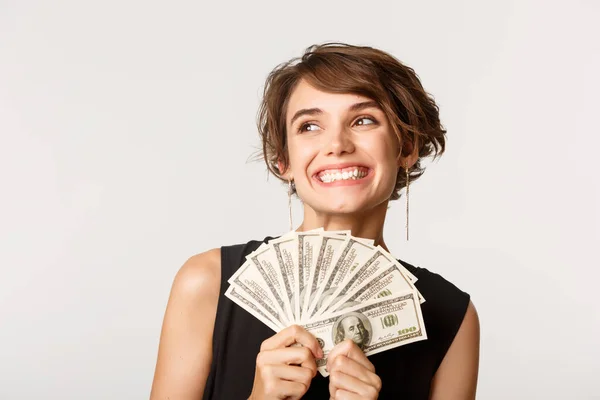 Glad söt ung kvinna med pengar ser övre vänstra hörnet, står över vit bakgrund — Stockfoto