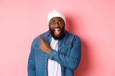 Şok olmuş ve baskı altında kalmış siyahi adam şikayet ediyor, kameraya bağırıyor ve sol üst köşedeki fotokopi alanını işaret ediyor, pembe arka planda duruyor.