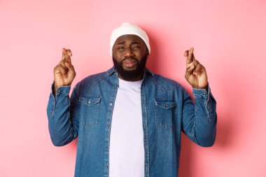 Genç Afro-Amerikan bir adamın mızmızlanması, tanrıya yalvarması, dua etmesi ve ağlaması, pembe arka planda dikilmesi.