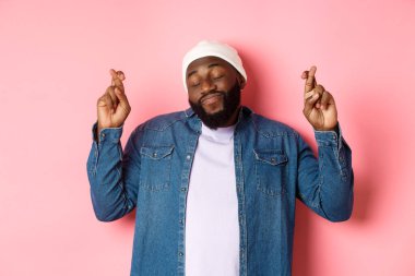 Umutlu ve hayalperest siyah adam dilek diliyor, dua ediyor ve gülümsüyor, pembe arka planda duruyor.