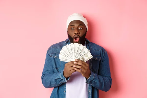 Incroyable homme afro-américain recevoir un prix en espèces, montrant de l'argent et regardant dans la crainte, debout sur fond rose — Photo