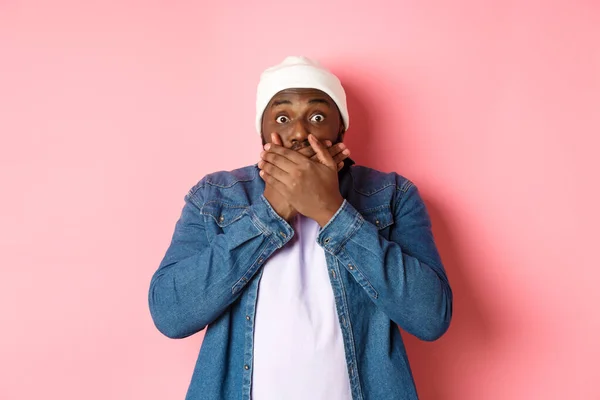 Σοκαρισμένος αφροαμερικάνος καλύπτει το στόμα και κοιτάζοντας την κάμερα, στέκεται άφωνος σε ροζ φόντο — Φωτογραφία Αρχείου