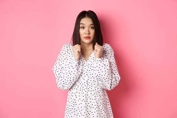 Angst vor süßen asiatischen Mädchen im Kleid, die besorgt aussehen, sich ängstlich fühlen und nervös in die Kamera starren, vor rosa Hintergrund stehen — Stockfoto