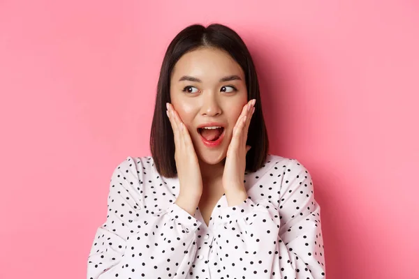 Primer plano de hermosa mujer asiática mirando sorprendido y emocionado, escuchar noticias increíbles, mirando a la izquierda y regocijándose, de pie sobre fondo rosa —  Fotos de Stock
