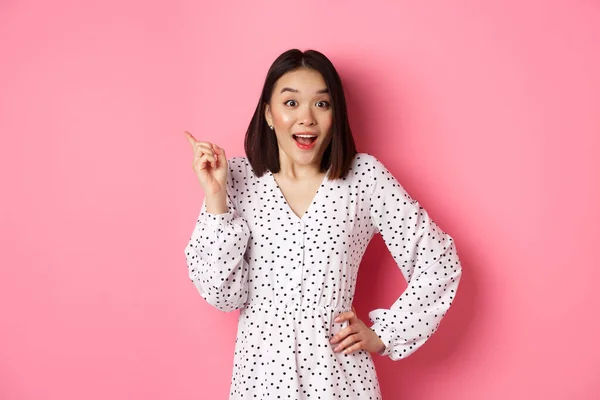 Χαριτωμένη Ασιάτισσα με φόρεμα που δείχνει το πάνω αριστερό μέρος της γωνίας. Κορεάτικο μοντέλο δείχνει διαφήμιση, στέκεται πάνω από ροζ φόντο — Φωτογραφία Αρχείου