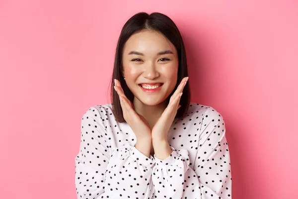 Bellezza e cura della pelle concetto. Primo piano di carino asiatico donna mostrando pulito perfetto viso e sorridente, guardando felice a macchina fotografica, in piedi su sfondo rosa — Foto Stock