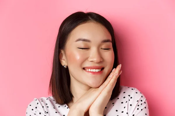 Concept beauté et soin de la peau. Headshot de femme asiatique adorable et rêveuse yeux fermés, souriant nostalgique, debout sur fond rose — Photo