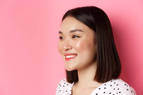 Conceito de beleza e cuidados com a pele. Perfil de bela menina asiática sorrindo e olhando feliz esquerda, de pé contra fundo rosa — Fotografia de Stock