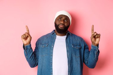 Üzgün ve kasvetli, bereli Afro-Amerikan adam, parmaklarını havaya kaldırıyor, iç çekiyor ve üzüntü ile en üste bakıyor, pembe arka planda duruyor.