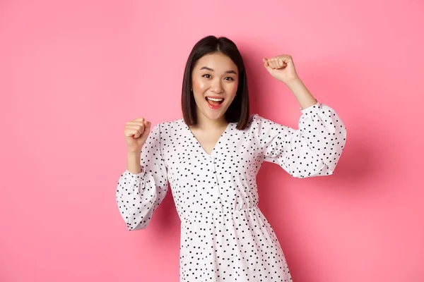 Mulher coreana bonita dançando e se divertindo, sorrindo feliz para a câmera, posando contra fundo rosa — Fotografia de Stock