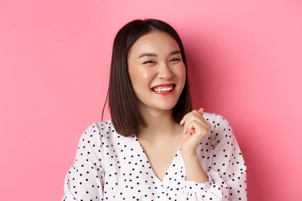 Conceito de beleza e estilo de vida. Close-up de feliz asiático fêmea rindo, olhando feliz e mostrando emoções genuínas, de pé sobre fundo rosa — Fotografia de Stock