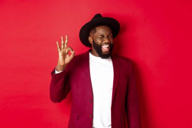 Noel alışverişi ve insanların konsepti. Yakışıklı siyah adam kendine güvenerek işaret veriyor, garanti veriyor, evet diyor, kırmızı arka planda duruyor.