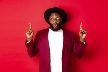 Kış tatili ve alışveriş konsepti. Adam şaşkın şaşkın bakıyor ve kırmızı arka planda duran reklam teklifini işaret ediyor.