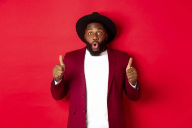 Noel alışverişi ve insanların konsepti. Yakışıklı siyah adam tatmin olmuş gülümsüyor, onaylıyor ve onaylıyor, kırmızı arka planda duruyor.