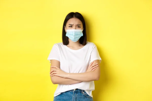 Covid, conceito de saúde e pandemia. Mulher asiática em t-shirt branca e máscara médica cruzar os braços no peito e olhando triste e decepcionado com a câmera — Fotografia de Stock