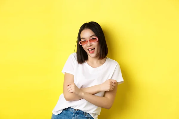 Conceito de moda e estilo de vida. Sassy e confiante mulher asiática na moda óculos de sol olhando auto-confiante para a câmera, de pé sobre fundo amarelo — Fotografia de Stock