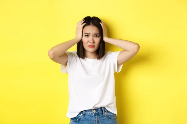 Donna asiatica che si tiene per mano e sembra triste, avendo un problema, in piedi ansioso contro sfondo giallo — Foto Stock