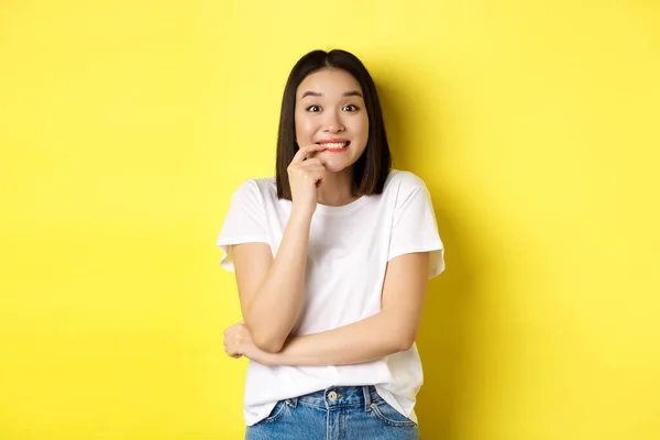 Retrato de menina asiática alegre quer algo, olhando com desejo e tentação para a câmera, sorrindo para a câmera, de pé ovr fundo amarelo — Fotografia de Stock