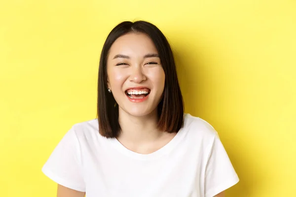 Close up de feliz jovem mulher se divertindo, sorrindo e rindo despreocupado, de pé em t-shirt branca sobre fundo amarelo — Fotografia de Stock