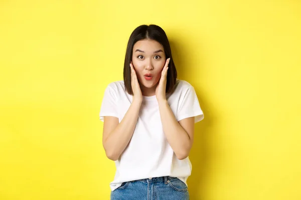Krása a módní koncept. Asijské dívka říká wow s úžasem, kontrolu úžasné promo dohoda, stojící nad žlutým pozadím — Stock fotografie