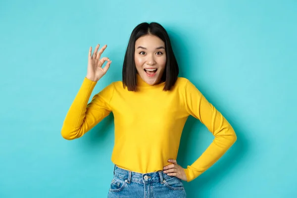 Menina coreana incrível mostrando gesto ok e sorrindo para a câmera, aprovar e recomendar oferta especial, de pé sobre fundo azul — Fotografia de Stock