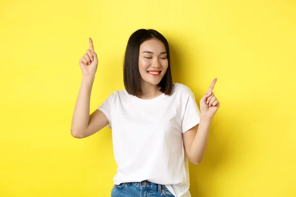 Feliz mulher asiática dançando e se divertindo, posando em camiseta branca contra fundo amarelo — Fotografia de Stock