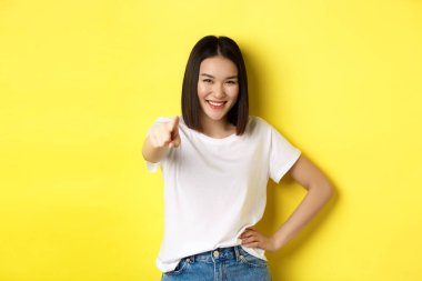 Sana ihtiyacımız var. Kendine güvenen Asyalı kadın gülümsüyor, kamerayı işaret ediyor, ona katılmaya davet ediyor, işaret ediyor ya da sarı arka planda duran birini seçiyor.