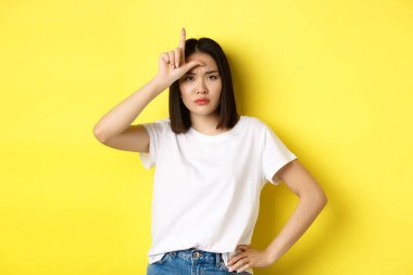 Ciddi ve kibirli Asyalı kadın kayıp takımla alay ediyor, alnında ezik işareti olan, kendine güvenen, sarı arka planda duran, kameraya bakan