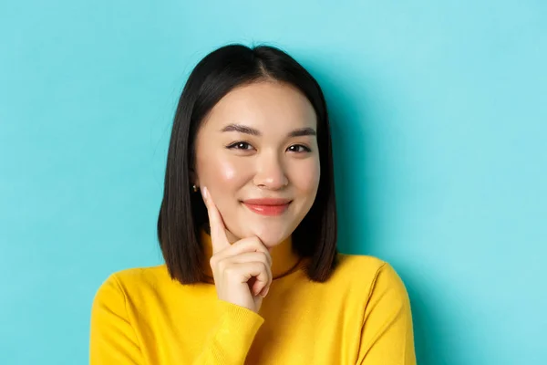 Güzellik ve makyaj konsepti. Düşünceli Asyalı kadının kameraya bakıp gülümsemesi, bir fikri olması, mavi arka planda durması. — Stok fotoğraf
