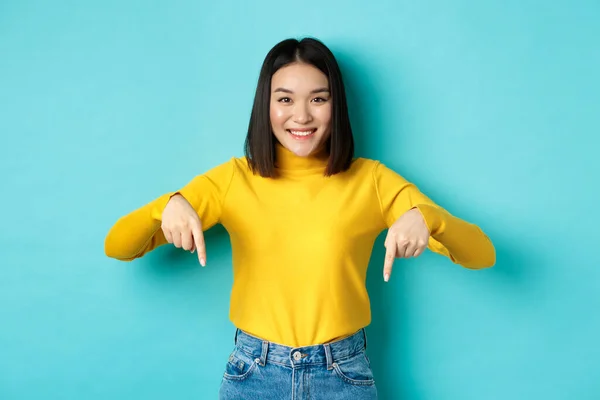 Köpkoncept. Vacker koreansk tjej med glatt leende, pekande fingrar mot banner, stående mot blå bakgrund — Stockfoto