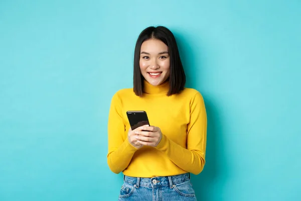 Vacker och elegant asiatisk kvinna shopping online på mobiltelefon, står över blå bakgrund — Stockfoto