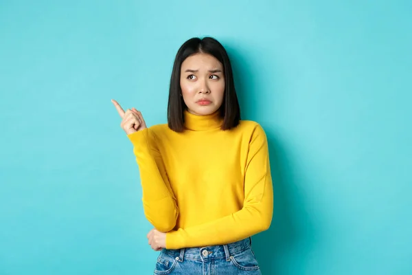 쇼핑 컨셉. 실망하고 우울 해 하는 아시아 여인이 화를 내며 나쁜 뉴우스 깃발을 손가락으로 가리키며 푸른 배경 위에서 있는 모습 — 스톡 사진