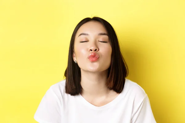 Concept de Saint Valentin. Gros plan de mignon asiatique fille pucker lèvres et fermer les yeux pour baiser, debout romantique sur fond jaune — Photo