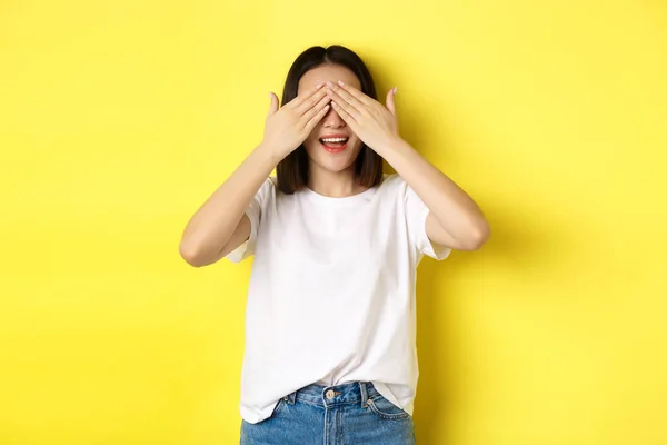 Boldog ázsiai nő vár meglepetés ajándék, csukott szemmel és mosolygó, vár valamit, áll a sárga háttér — Stock Fotó