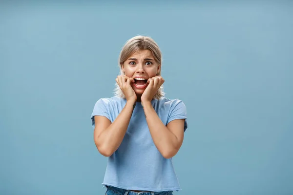 Indoor shot of shocked troubled girlfriend hearing mom returned home being with boyfriend biting fingernails being in helpless perplexed situation feeling anxious and scared over blue background — Foto de Stock