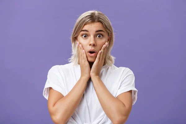 Taille-up shot van verbluft onder de indruk prachtig gebruinde vrouw in wit t-shirt met blond haar hijgend met geopende mond van verrassing hand in hand op wangen van verbazing en nieuwsgierigheid — Stockfoto