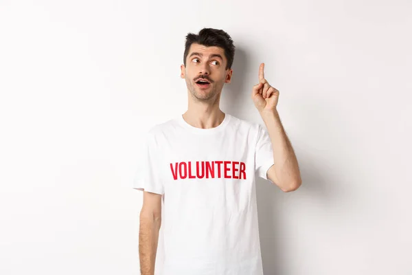 Bonito jovem em t-shirt voluntária ter uma ideia, levantando o dedo e dizendo sugestão, fundo branco — Fotografia de Stock