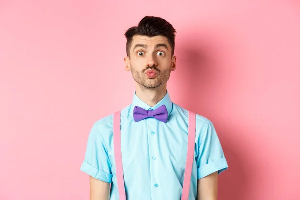 Joven divertido esperando un beso con labios hinchados y cara tonta, de pie sobre un fondo rosa romántico. Concepto de amor y día de San Valentín —  Fotos de Stock