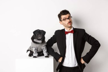 Hayvanlar, parti ve kutlama konsepti. Yakışıklı genç adam ve resmi takım elbiseli köpek yavrusu kameraya bakıyor, beyaz arka planda duruyorlar.