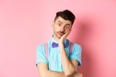 Shocked and tired caucasian guy staring pissed-off at camera, lean on palm and looking at something with skeptical face, standing over pink background