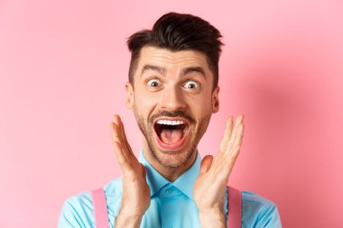 Mutlu beyaz adamın sevinç ve şaşkınlık çığlıkları attığı yakın plan, reklamları kontrol eden, pembe arka planda duran, havalı bir şey gören