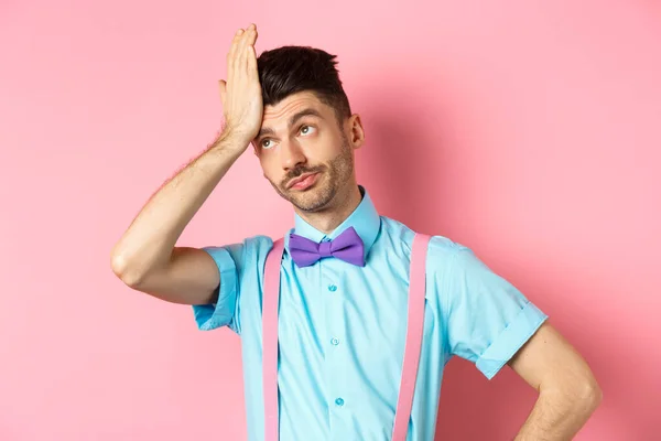 Annoyed guy with suspenders and bow-tie, facepalm with eyes rolled up, standing irritated by something stupid, standing over pink background — Stock Photo, Image