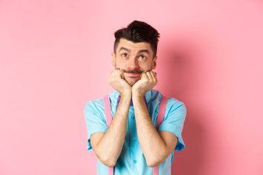 Aptal genç adam ellerini kaldırıp yukarı bakıyor, bir şeyin hayalini kuruyor, pembe arka planda bir şeyler canlandırıyor.