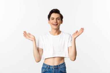 Lgbtq ve gurur konsepti. Mutlu ve tatmin olmuş genç gay adam topaç üstünde alkışlıyor gururla el çırpıyor, kameraya gülümsüyor, beyaz arka planda duruyor.