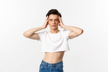 Lgbtq ve gurur konsepti. Güzel ve kendine güveni tam bir eşcinsel. Kırpılmış bluz giyiyor, yüzüne dokunuyor ve kameraya küstah bakıyor. Beyaz arka planda duruyor.