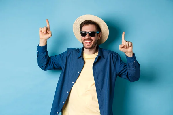 Munter fyr med stråhatt og solbriller, danser og har det gøy på ferie, står over blå bakgrunn. Sommerturistbegrepet – stockfoto